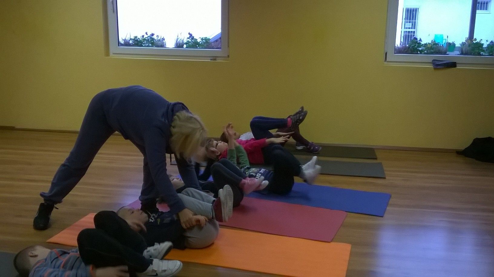 Tammy a hanyatt fekvő gyerekek lábát tartja egy szőnyeges gyakorlat közben