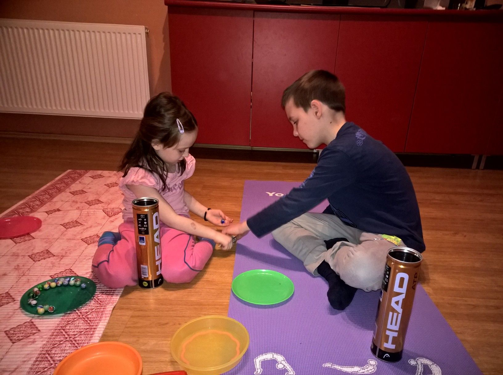 Két gyerek a jógaszőnyegen apró tárgyakat válogat tányérok és dobozok között