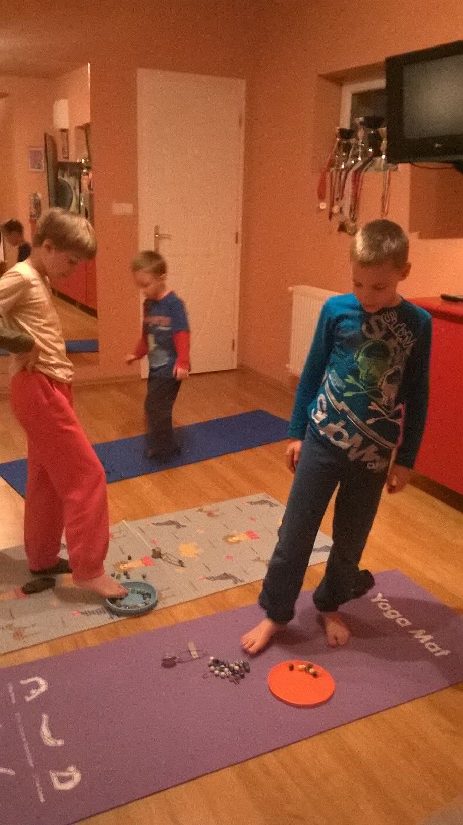 Mezítlábas gyerekek a tornaszőnyegen, előttük színes apró tárgyak és tányér