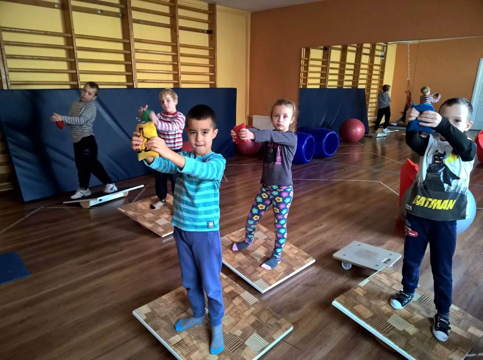 Gyerekek egyensúlyozó deszkákon állnak, kezükben plüssfigurát tartanak